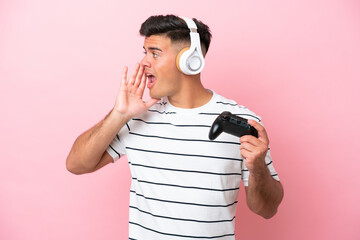 Young handsome man playing with a video game controller isolated on pink background shouting with mouth wide open to the side © luismolinero