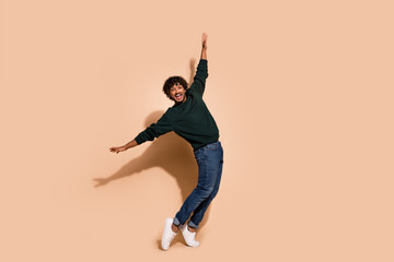 Full size photo of nice young man stand tiptoe dance wear sweater isolated on beige color background