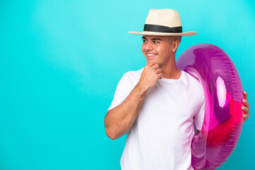 Young caucasian man holding air mattress isolated on blue background thinking an idea and looking...