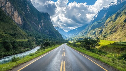 A scenic asphalt highway through a lush valley, with mountains rising on both sides and a river running alongside the road.