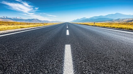 Fototapeta premium A smooth asphalt highway stretching into the distance under a clear blue sky, with mountains visible on the horizon.