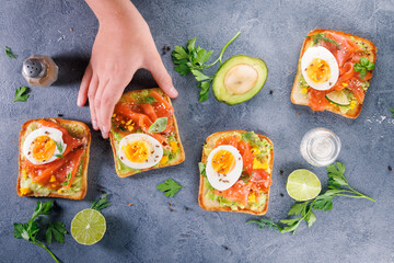 Top view of toast with avocado, smoked salmon, and egg, with a hand picking up a piece. Ideal for...