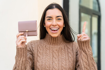 Young woman holding a wallet at outdoors pointing up a great idea