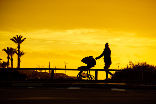 Silhouette of woman with baby stroller walking on beach at sunset