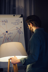 A conspiracy theorist stands with a floor lamp in his hand near a flipchart with notes. The concept...