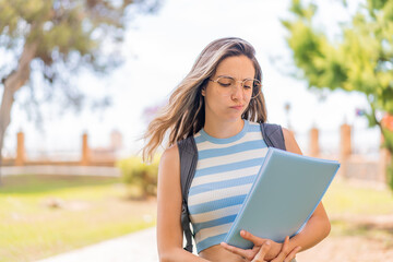 Young pretty student woman at outdoors with sad expression