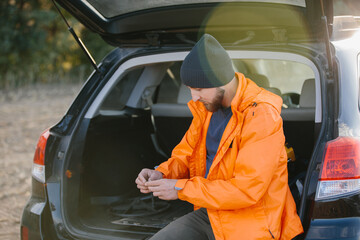 A male archaeologist sits in the trunk of a car holding ancient coins found with a metal detector.