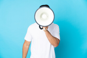 Caucasian man over isolated blue background shouting through a megaphone to announce something