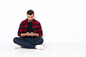 Young handsome man sitting on the floor sending a message with the mobile