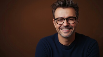 Obraz premium Friendly Gentleman with Glasses Smiling Confidently at the Camera in Casual Attire on Brown Background