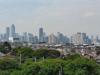 Obraz premium The photo showcases a contrast between a dense urban slum area in the foreground and a modern skyline of tall skyscrapers in the background, under a cloudy sky.