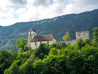 Ringgenberg castle church, old traditional buildings on the green trees hill near Lake Brienz in the morning, and mountain and cloudy summer sky background, view from cruise travel, Switzerland.