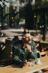 Toughtful man savoring coffee alone at a cozy cafe on a sunny day while lost in contemplation by the window