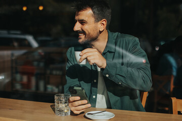 Toughtful man savoring coffee alone at a cozy cafe on a sunny day while lost in contemplation by the window