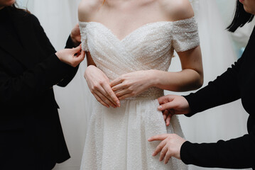 wedding salon administrators adjust bride dress at fitting in salon, cropped, no face, preparing to...
