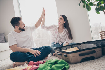 Full size photo of two people pack suitcase prepare travel give high five living room flat indoors