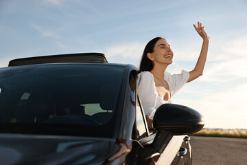 Smiling young woman leaning out of car window outdoors. Enjoying trip