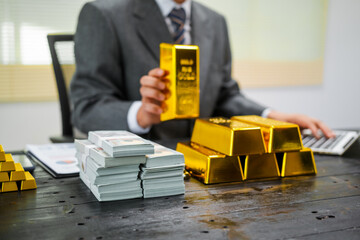 Businessman in suit sits at his desk, holding a shining gold bar. financial charts, the scene...