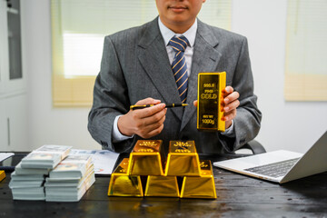 Businessman in suit sits at his desk, holding a shining gold bar. financial charts, the scene...