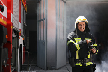 Obraz premium Portrait of firefighter in uniform with high pressure water jet near fire truck outdoors