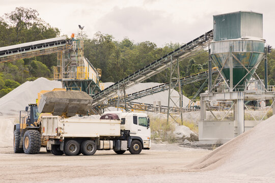 Loader and tipper truck at a quarry site with machinery in background
