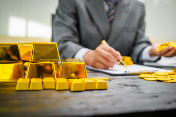 Businessman in suit sits at his desk, holding a shining gold bar. financial charts, the scene symbolizes wealth, investment success, growing influence of cryptocurrency and blockchain.