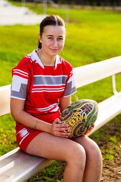 Portrait of young aboriginal teen footy player with football sitting on sidelines of playing field