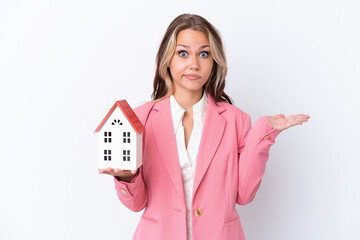 Real estate Russian agent holding a toy house isolated on white background having doubts while raising hands