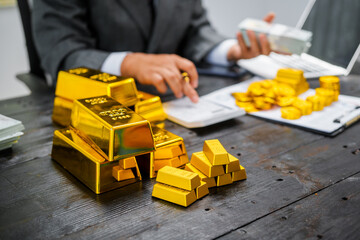 Obraz premium Businessman in suit sits at his desk, holding a shining gold bar. financial charts, the scene symbolizes wealth, investment success, growing influence of cryptocurrency and blockchain.