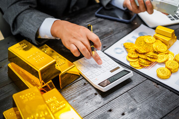 Businessman in suit sits at his desk, holding a shining gold bar. financial charts, the scene...