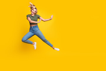 Full size photo of positive girl dressed khaki crop top jeans jump out of object in empty space isolated on yellow color background