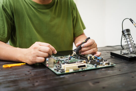 Technician carefully repairs a computer circuit board, using precision tools to address hardware issues. technical expertise needed for troubleshooting and upgrading electronic systems in workspace.
