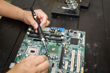 Technician carefully repairs a computer circuit board, using precision tools to address hardware...