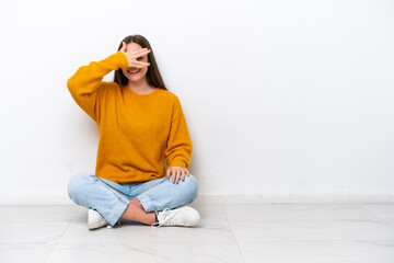 Young girl sitting on the floor isolated on white background covering eyes by hands and smiling