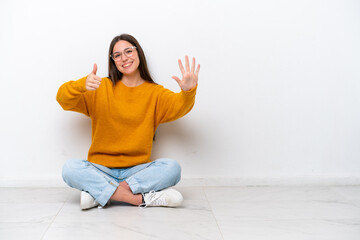 Young girl sitting on the floor isolated on white background counting six with fingers