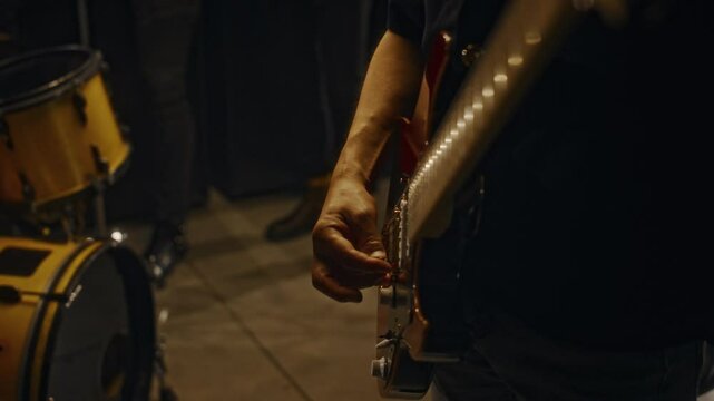 Close-up of hands of anonymous male musician strumming electric guitar while standing in recording studio with bandmates before jam session