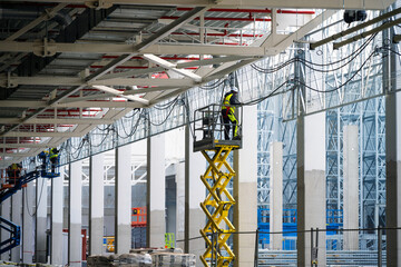 Electricians installing cables on cable trays working at height on construction site