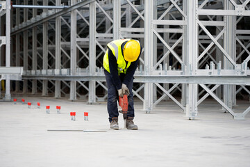 Worker drilling holes for chemical anchors in concrete foundation slab on construction site of...