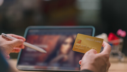 People shopping online using tablet concept. Close-up of person holding gold credit card and digital pen, ready to engage in online shopping on tablet in cozy environment