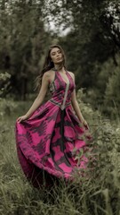 Fototapeta premium Elegant Woman in Flowing Pink Dress Against a Lush Green Background