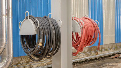 Hoses Wrapped Around Metal Stands. Two hoses, one black and one red, are neatly coiled around metal stands attached to a wall.