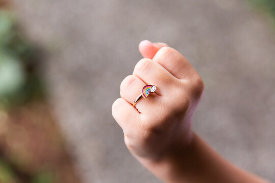 Close up photo of a hand with a rainbow ring worn around the finger