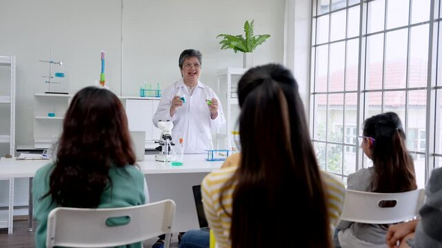 Elderly teacher teaches science course, holding laboratory flask in both hands, stand talk with students in class, summarize results experiment before class, make students understand experiment more.