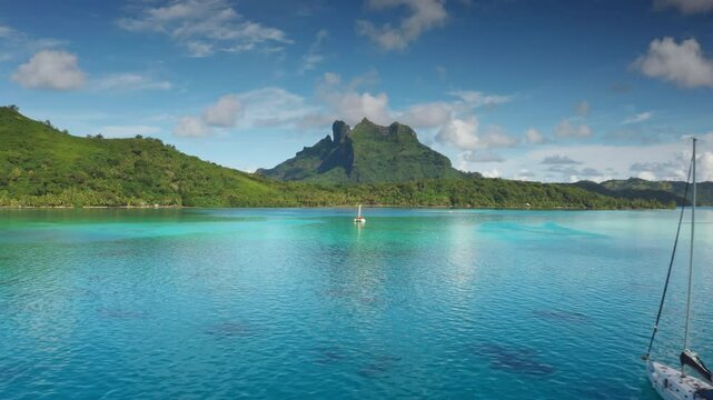 Remote luxury yacht travel to Bora Bora island, French Polynesia. Wild nature paradise, turquoise lagoon water, green mountain. Popular tourist destination, exotic summer vacation. Aerial drone flight