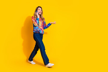 Full size photo of pretty young girl talk phone call walking wear trendy colorful outfit isolated on yellow color background