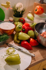 preparing stuffed peppers with rice and herbs, close-up of green pepper on white plate, fresh vegetables and ingredients on kitchen table, cooking process