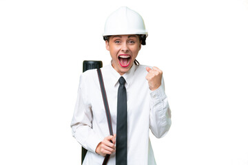 Young architect woman with helmet and holding blueprints over isolated background celebrating a victory in winner position