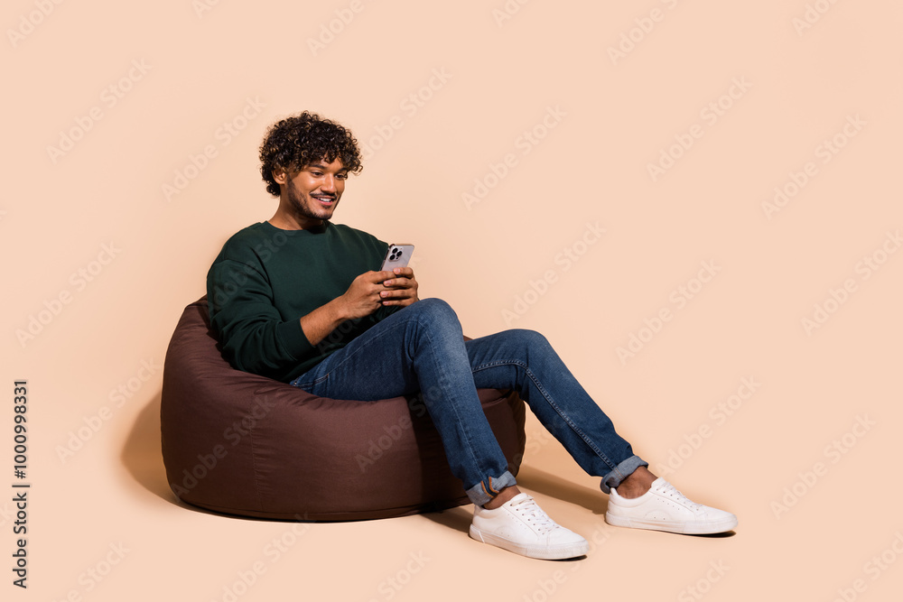 Wall mural Full length photo of handsome good mood guy wear sweatshirt communcating gadget emtpy space isolated beige color background