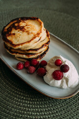 stack of homemade pancakes with whipped cream and fresh cranberries on ceramic plate, placed on green woven placemat in cozy kitchen setting