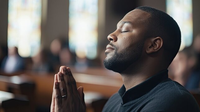 African American young man praying in joined hands and closed eyes.